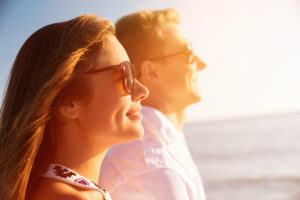 Young couple wearing sunglasses and looking out to sea.