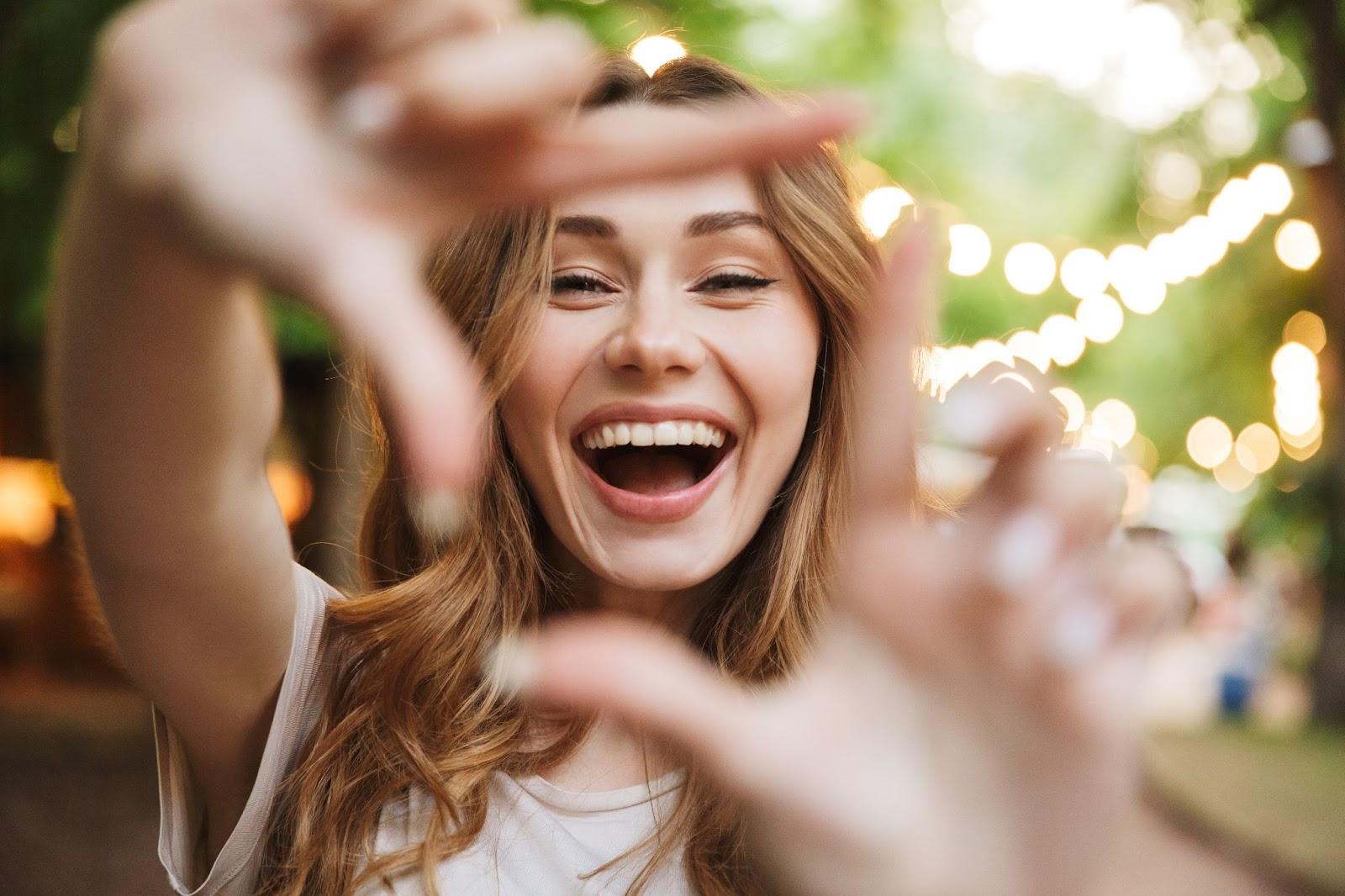 happy young girl showing frame with fingers while standing at the park