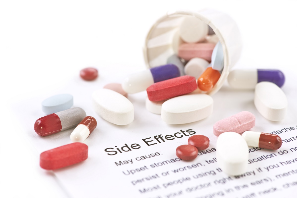 Assorted pills and capsules with side effects information sheet.