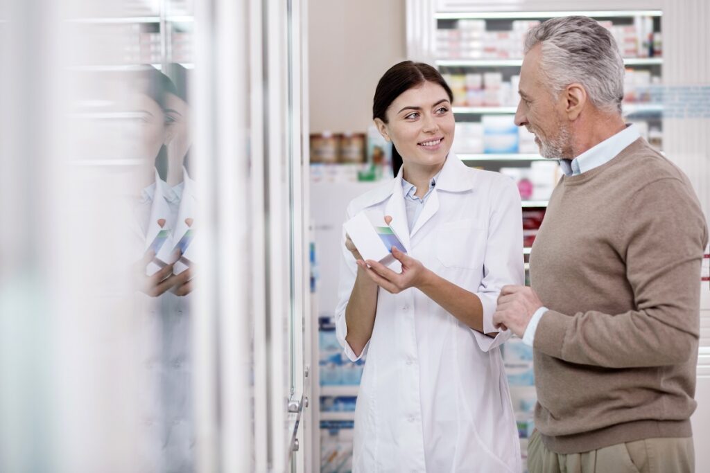 Joyful female pharmacist explaining mature man side effect while carrying medication