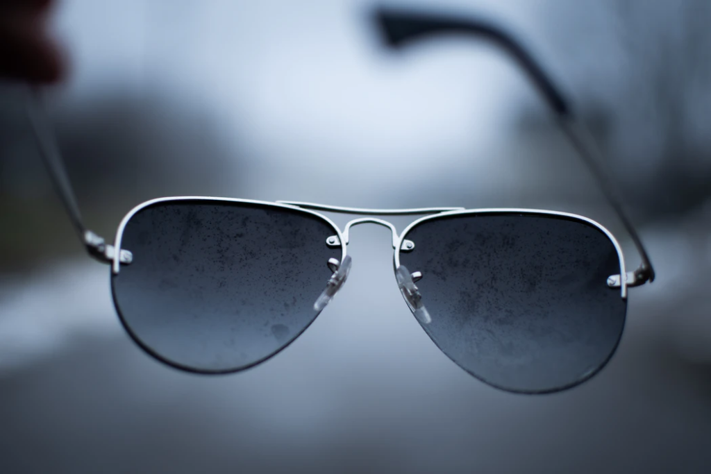 man holding sunglasses with water on them on a rainy day